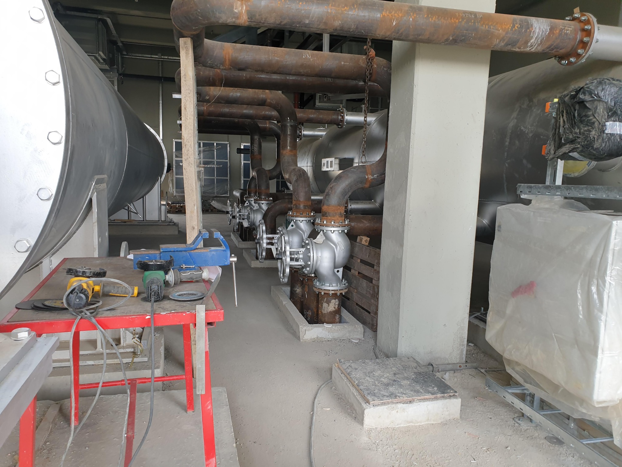 Scule și masă de lucru între conducte, armături și echipamente industriale.