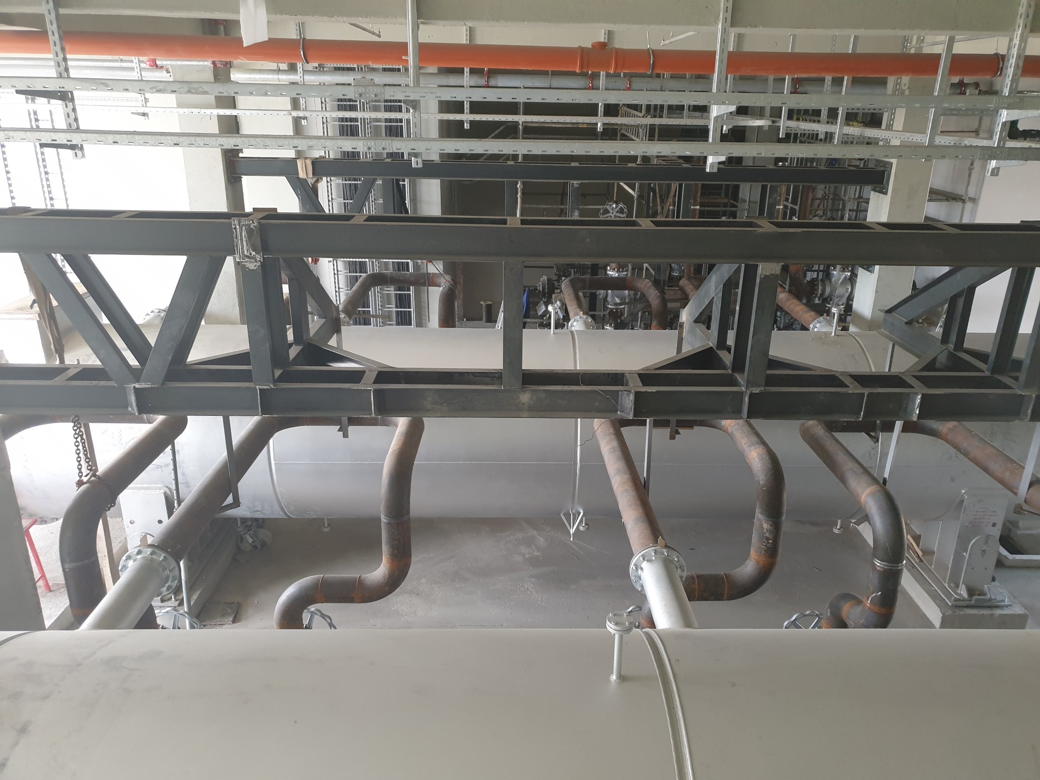 Trasee de conducte amplasate sub o structură metalică, văzute de sus.