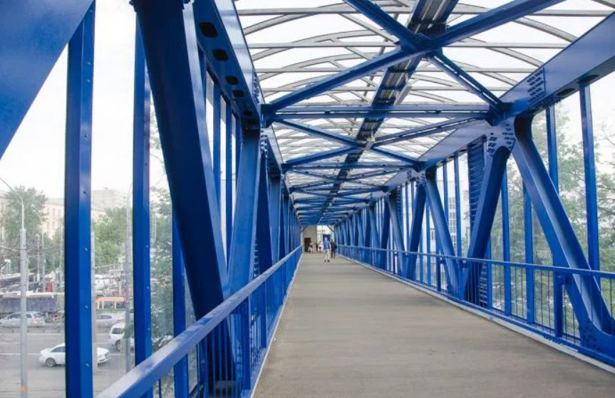 Interior de pasarelă pietonală cu grinzi, contravântuiri și balustrade albastre